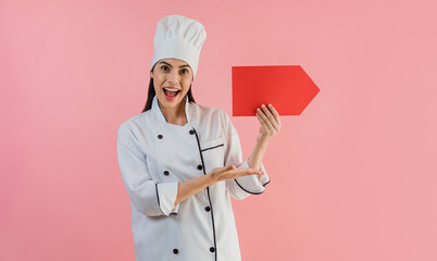 Portrait of young latin woman with chef hat holding a banner and copy space on a pink background in latin America