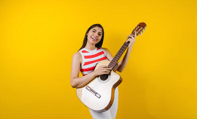 portrait of young latin woman holding a guitar on music concept and copy space on yellow background in Latin America
