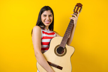 portrait of young latin woman holding a guitar on music concept and copy space on yellow background...