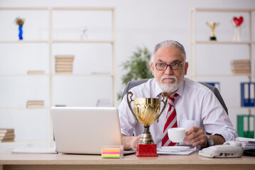 Old male employee being awarded with golden cup