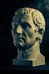 Bronze color gypsum copy of ancient statue of Guy Julius Caesar Octavian Augustus head for artists on dark textured background. Renaissance epoch. Plaster sculpture of man face.Template for art design - obrazy, fototapety, plakaty