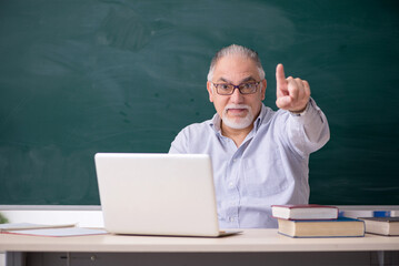 Old male teacher in front of green board