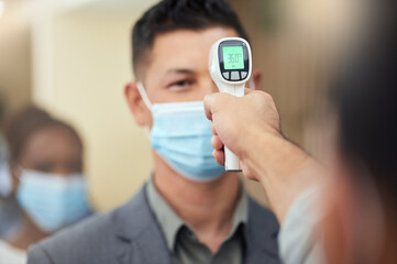 It's the new normal. Cropped shot of a handsome mature businessman wearing a mask and having his temperature taken while standing at the head of a queue in his office.