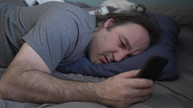 Tired Man in Bed With Smartphone Falling Asleep