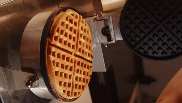 The cook in the kitchen opens a waffle iron with ready-made golden baked delicious waffles. Vertical video for smartphone screen with baking viennese waffles dessert pancake