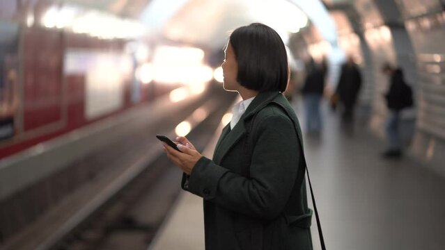 Successful african american female using smartphone at metro subway platform waiting for train. Successful businesswoman or business owner using mobile phone while riding to office or home