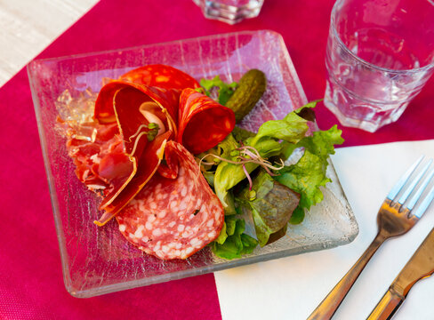 Appetizing assorted meat of smoked sausage and sliced carbonad, served with pickled cucumbers and lettuce