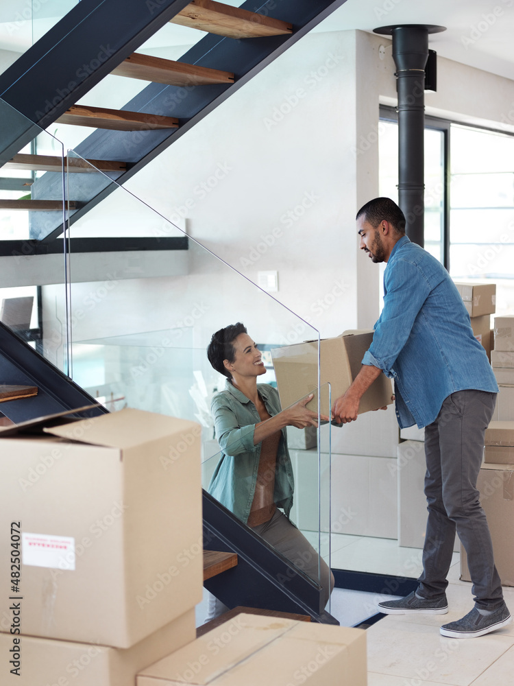 Poster Is this the last of them. Shot of a happy young couple passing boxes to each other while moving into their new home.