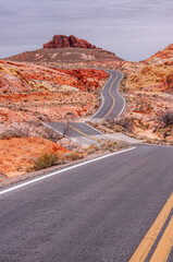 Overton, Nevada, USA - February 24, 2010: Valley of Fire. Portrait landscape of gray asphalt road with yellow divider meandering upwards among multi-color desert floor towards red rock.