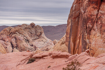 Fototapeta na wymiar Overton, Nevada, USA - February 24, 2010: Valley of Fire. Detail of red and beige rocks with dry desert on horizon under heavy rainy gray cloudscape.