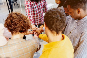 Multiracial group of men and women, co-workers, joining hands in a sign of union and diversity in a co-working office.