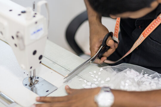 Male dressmaker cutting fabric on the sewing machine with scissor at the workshops. 