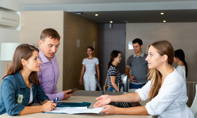 Smiling young diligent woman assistant of notary public receiving customers in hall of modern office