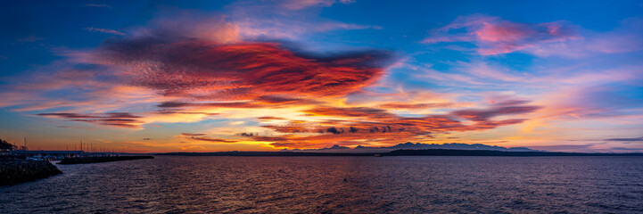 A panorama with Colorful clouds and an overcast sky at sunset with the ocean in the foreground and mountains in the background