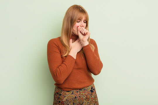 redhead pretty woman feeling ill with a sore throat and flu symptoms, coughing with mouth covered