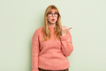redhead pretty woman looking astonished in disbelief, pointing at object on the side and saying...
