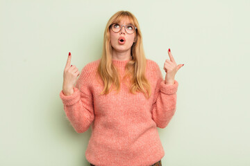 redhead pretty woman feeling awed and open mouthed pointing upwards with a shocked and surprised...