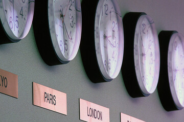 Row of various time zone clocks with placard text on wall at office