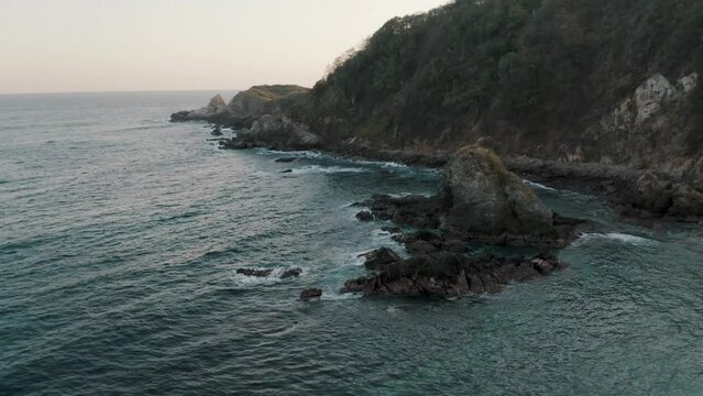 Aerial orbit shot of a big rock formation on the coastline of Zipolite, Oaxaca, Mexico on a cloudy day.