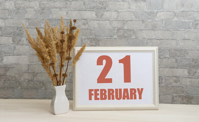 february 21. 21th day of month, calendar date.  White vase with ikebana and photo frame with...