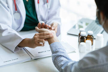 Woman doctor talks to female patient in hospital office while examining the patients pulse by...