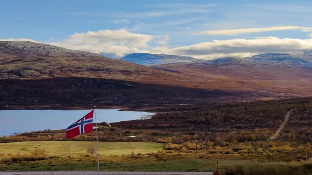 Norwegian flag waving in the mountains with a lake in the background.