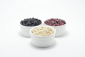 Frijoles negros blancos y rojos dentro de un tazón sobre fondo blanco. Alimento consumido en...