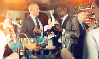 Two glad positive smiling male colleagues enjoying corporate bar party, drinking beer and having fun conversation