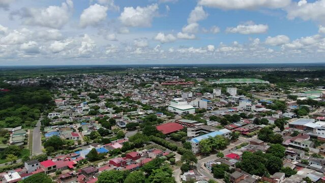 Car driving over the gray road in the big stretched city of Yopal with multple green trees in the neighborhood on a partly cloudy day. Wide drone shot