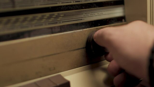 Tuning for radio station in vintage 1960s receiver, close up of hand on wheel, full frame