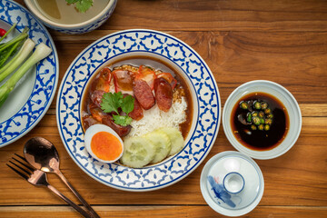 Rice with red roasted pork with sauce and Egg topped in a white dish on wooden table.