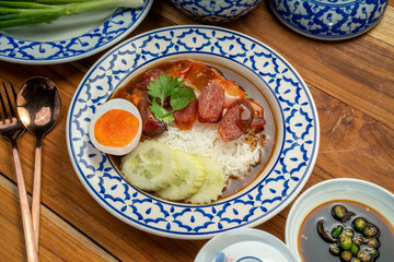 Rice with red roasted pork with sauce and Egg topped in a white dish on wooden table.
