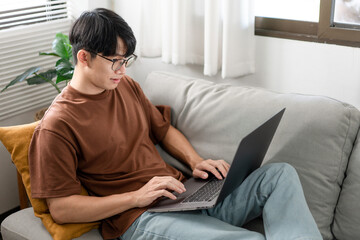 Technology Concept The man that is putting on glasses leaning his back on the dark yellow while focusing on the laptop’s screen