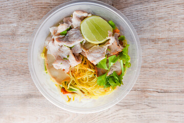 Top view Thai and China Asian food yellow noodles lemon lime, Dry noodles pork with red roasted pork and vegetable in plastic bowl on wooden table
