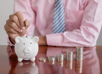 The hand of a businessman puts coins in a piggy bank, saves money with coins, steps into a...