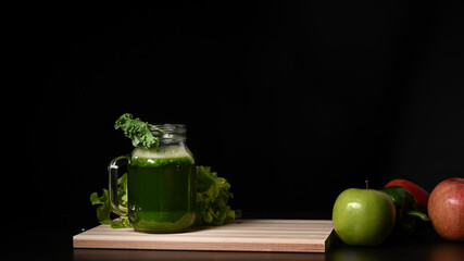 Green vegetable smoothie in glass with vegetables and fruits on wooden table.