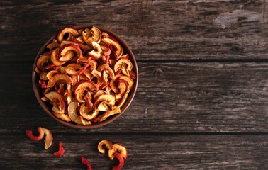 dried apple slices in a brown dish on a dark wooden background