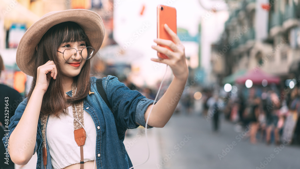 Wall mural Young adult asian woman traveller selfie by mobile phone wear backpack chinatown street food market backgprund.