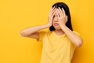 woman with Asian appearance in a yellow t-shirt holding his head discontent yellow background unaltered