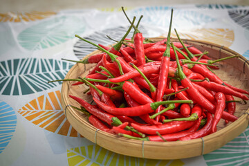 Close-up of stacked fresh red peppers with stems on a bamboo basket.
