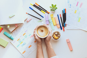 Student planning process. The student's desk with a weekly schedule, books, colorful markers and hands with a cup of coffee. View from above.