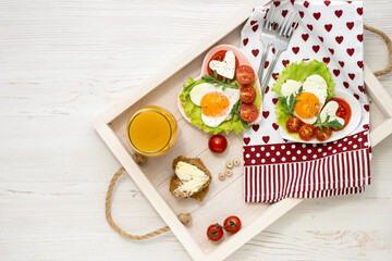 Valentine's Day breakfast for two people on a wooden tray. Heart-shaped plates with fried eggs, tomatoes and cheese, juice and coffee. View from above. Space for text.