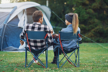 Young nice couple sitting on chairs inf front of tent on camping