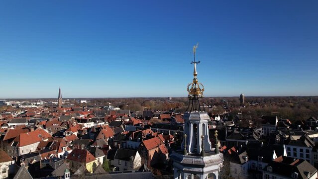 Rotating movement around wind gauge ornament op top of Walburgiskerk church in picturesque tower town of Zutphen in The Netherlands. Aerial architectural detail of religious building against blue sky.