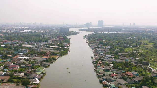Aerial top view of residential local houses with Phasi Charoen, Chao Phraya canal or river, nature trees, Nonthaburi City, Thailand in urban city town in Asia, buildings.
