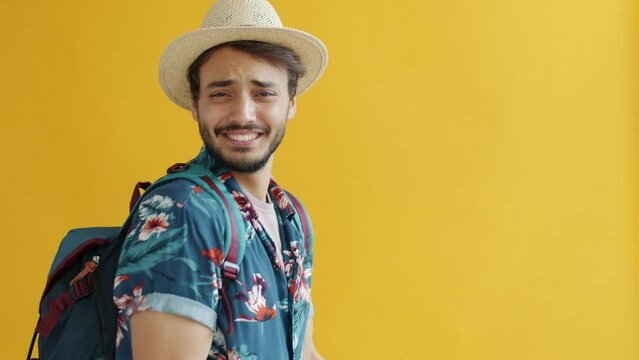 Portrait of happy Middle Eastern traveller with backpack speaking looking at camera inviting for adventure on yellow background. People and vacation concept.