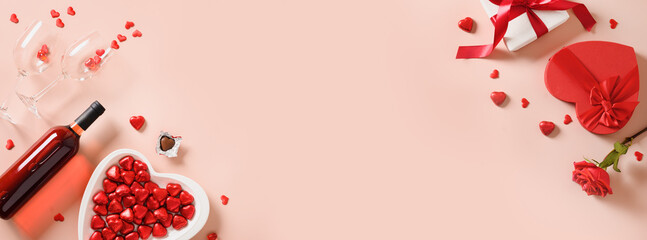 Valentine's day banner with red wine, gift, hearts chocolate sweets and red roses on pink background. View from above. Space for your greetings.