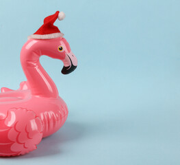 Pink inflatable flamingo with santa hat on a blue background. Minimal christmas layout © splitov27