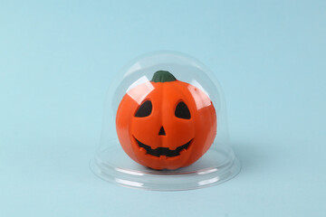 Halloween pumpkin jack under transparent dome on a blue background. Protection, isolation concept. Minimal layout