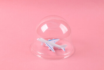 Air plane under transparent dome on pink background. Protection, travel isolation concept. Minimal layout